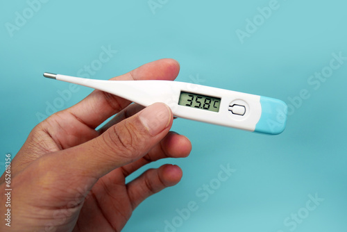 A man's hand holding a digital thermometer in her hand on a blue background. A person looks at an electronic thermometer with temperature. photo