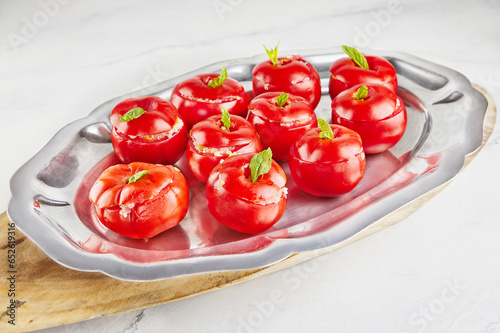 Stuffed tomatoes with basil leaf on board on light background © AlexanderD