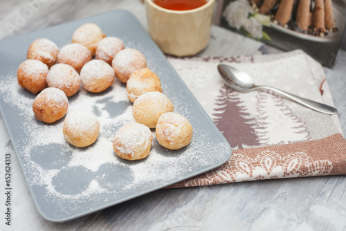 Curd donuts in powdered sugar on a plate, round donuts with a cup of tea