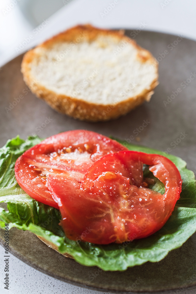 Closeup of burger buns layered with salad leaves and freshly salted tomato slices Closeup of burger buns layered with salad leaves and freshly salted tomato slices