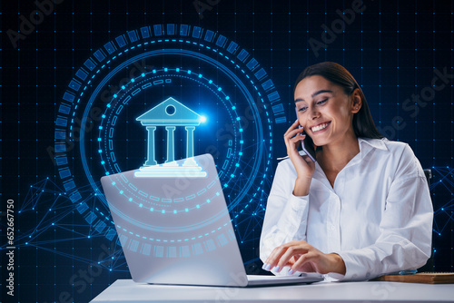 Attractive happy young european businesswoman using laptop and cellphone with creative round polygonal banking hologram on blurry background. Digital transformation and finance concept. photo