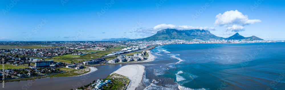 Fototapeta premium Panoramic view of the flooded Diep River flowing into Table Bay, carrying storm debris after a winter storm. Drone view, Table Mountain in background. 