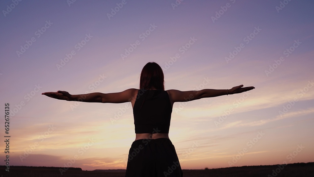 Happy woman with spread hands meditates outdoors under colorful sunset sky