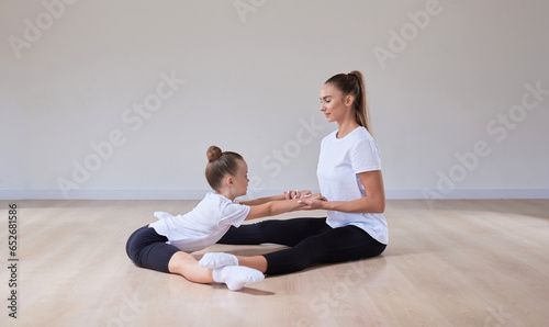 Beautiful female teacher helps a little girl stretch in a gymnastics class. The concept of education, sports, Pilates, stretching, healthy lifestyle.