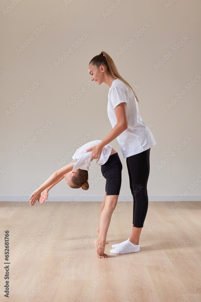 Beautiful female teacher helps a little girl stretch in a gymnastics class. The concept of education, sports, Pilates, stretching, healthy lifestyle.