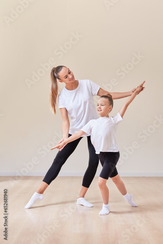 Beautiful woman teacher and a little girl perform dance movements in a bright studio. The concept of education, dance, sports, Pilates, stretching, healthy lifestyle.