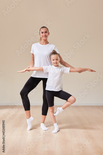 Beautiful woman teacher and a little girl perform dance movements in a bright studio. The concept of education, dance, sports, Pilates, stretching, healthy lifestyle.