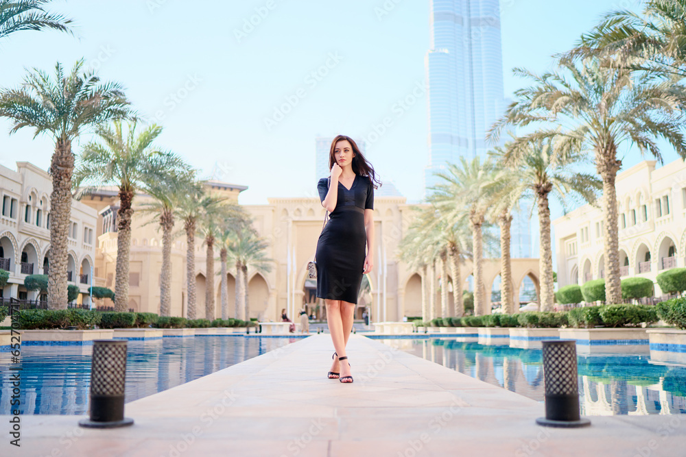Beautiful young woman with charming smile and long hair walking on Dubai Downtown.