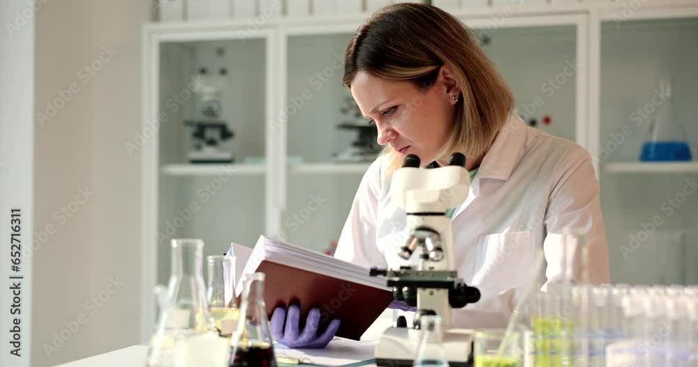 Scientist looks through a microscope and leafs through book. Chemical analysis of liquids with or forensic examination Scientist looks through a microscope and leafs through book. Chemical analysis of liquids with or forensic examination