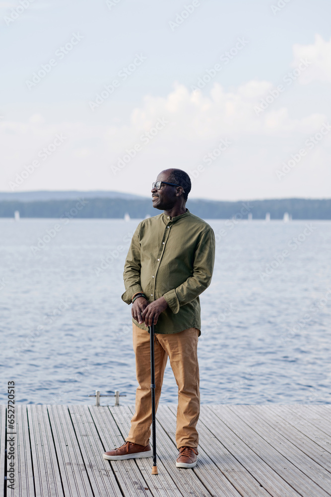 Vertical image of senior man with stick standing on pier against the lake Vertical image of senior man with stick standing on pier against the lake
