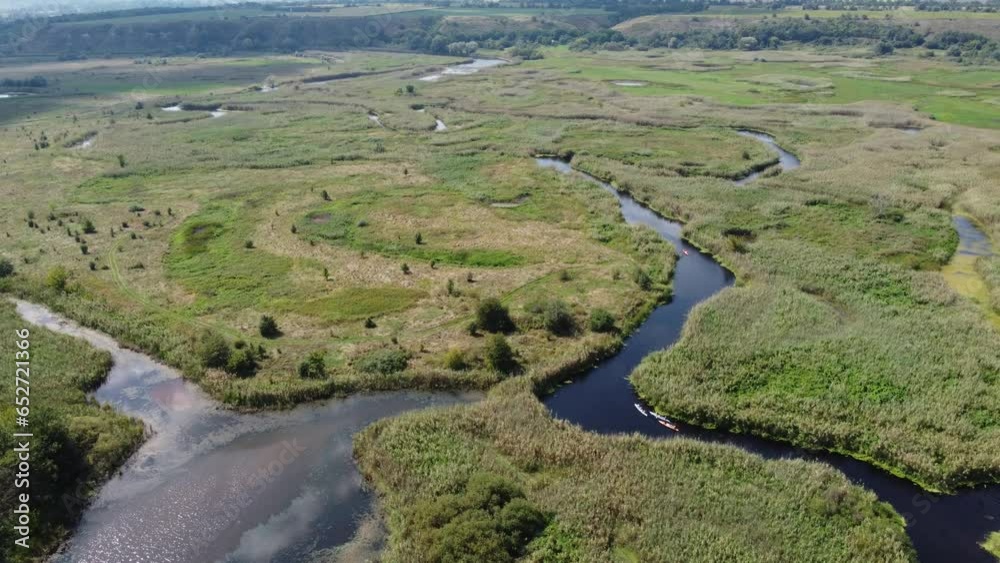 Drone view of a large swampy river valley with swamps, meadows and lakes. A small group of tourists in a canoe can be seen on the water. Drone view of a large swampy river valley with swamps, meadows and lakes. A small group of tourists in a canoe can be seen on the water.