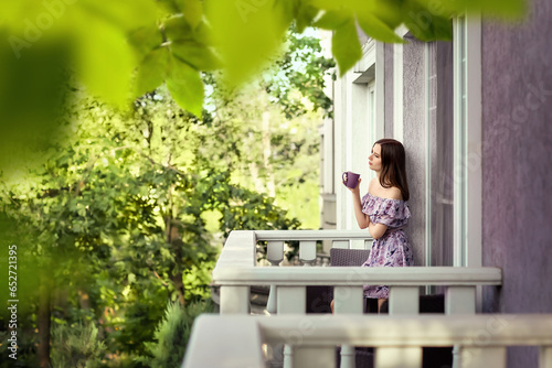 Wallpaper Mural A girl in a lilac dress stands on the balcony of her house. She is thoughtful, holding a mug of tea in her hands. Season of the year is summer. Torontodigital.ca