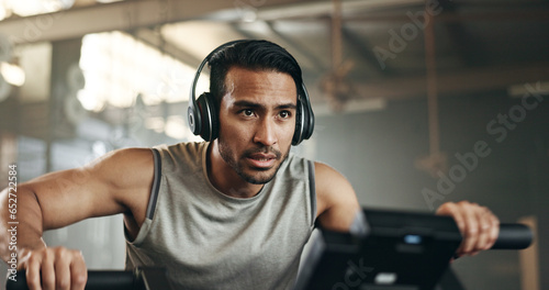 Asian man, headphones and cycling at gym on machine and listening to music in sports workout or exercise. Serious male person or athlete training on bicycle machine or equipment for healthy cardio photo