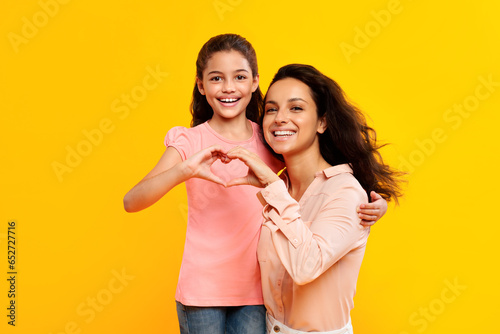 Smiling european mother and daughter showing heart symbol with fingers, connecting their hands together and smiling