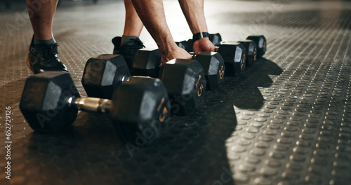 Fitness, athlete and closeup of dumbbells in gym for exercise, workout and sports training. Hands of strong bodybuilder lifting heavy weights on ground in wellness club for muscle, power or challenge photo