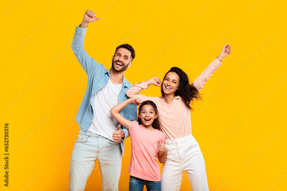 Victory concept. Overjoyed european family of three shaking clenched fists, making winner gesture over yellow background - obrazy, fototapety, plakaty 