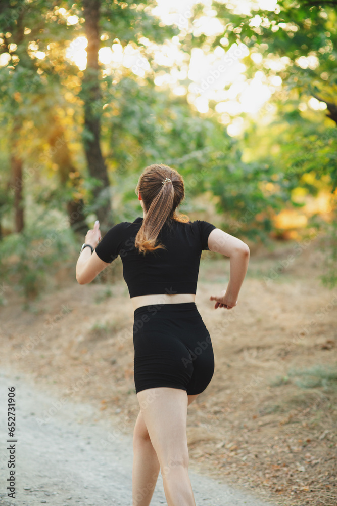 back of young running woman in forest park. Girl jogging at sunset on nature, health and sport concept back of young running woman in forest park. Girl jogging at sunset on nature, health and sport concept