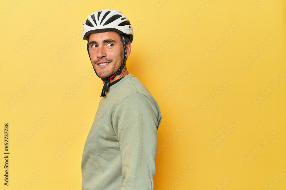 Fototapeta premium Casual dressed Latino cyclist on yellow looks aside smiling, cheerful and pleasant.