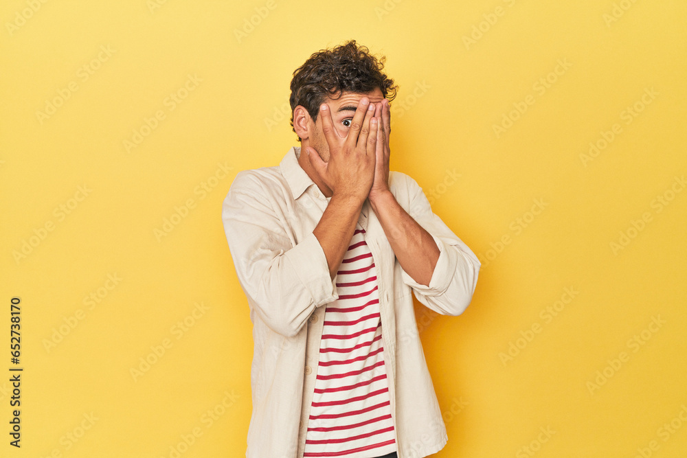 Young Latino man posing on yellow background blink through fingers frightened and nervous. Young Latino man posing on yellow background blink through fingers frightened and nervous.
