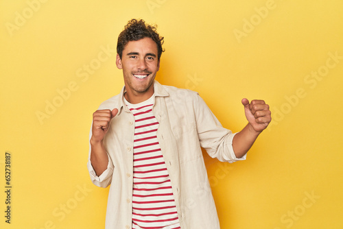 Young Latino man posing on yellow background dancing and having fun.
