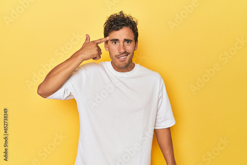 Young Latino man posing on yellow background showing a disappointment gesture with forefinger.