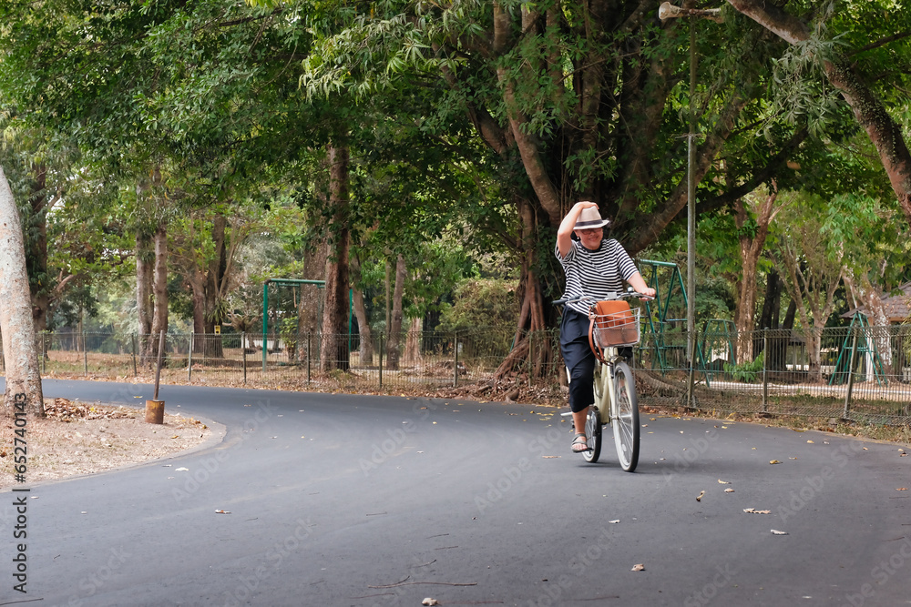 Woman riding bicycle under shady big trees in the park