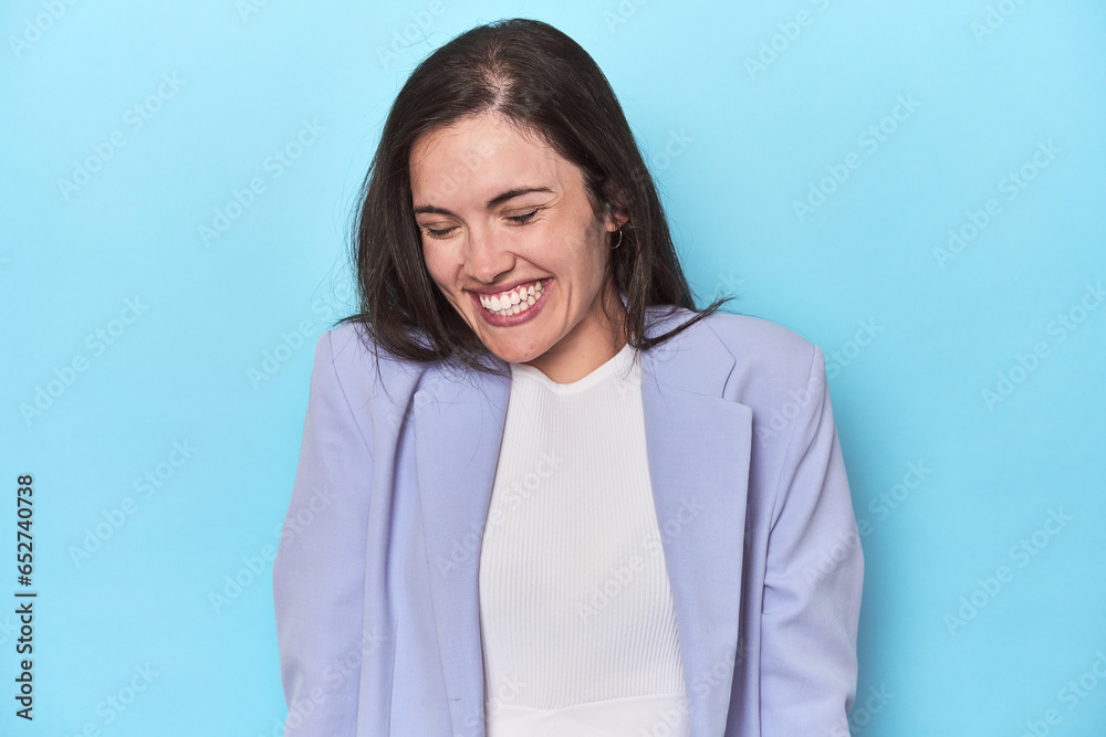 Woman in blue blazer on blue background laughs and closes eyes, feels relaxed and happy. Woman in blue blazer on blue background laughs and closes eyes, feels relaxed and happy.