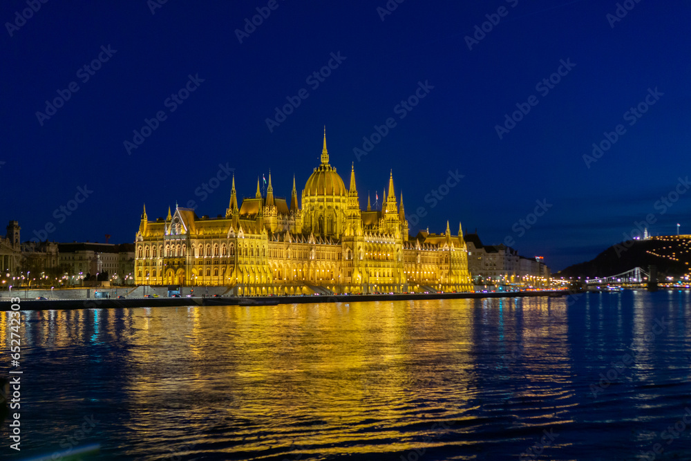 The Budapest Parliament building at night, with the Danube in the foreground