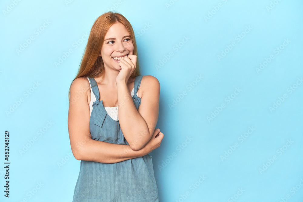 Redhead young woman on blue background relaxed thinking about something looking at a copy space.
