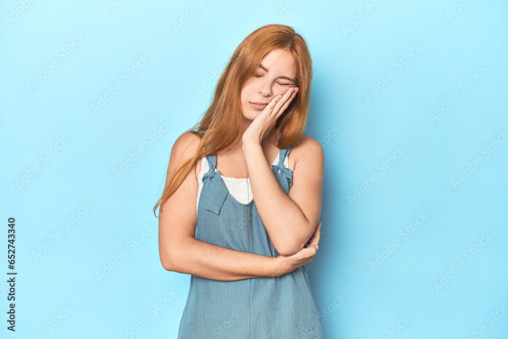 Redhead young woman on blue background who is bored, fatigued and need a relax day. Redhead young woman on blue background who is bored, fatigued and need a relax day.