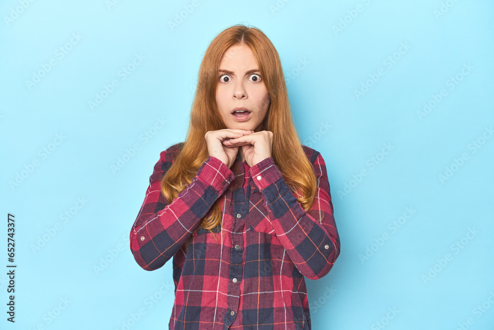Redhead young woman on blue background praying for luck, amazed and opening mouth looking to front. Redhead young woman on blue background praying for luck, amazed and opening mouth looking to front.