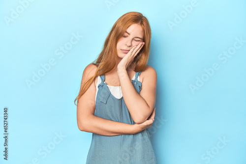 Redhead young woman on blue background who is bored, fatigued and need a relax day.