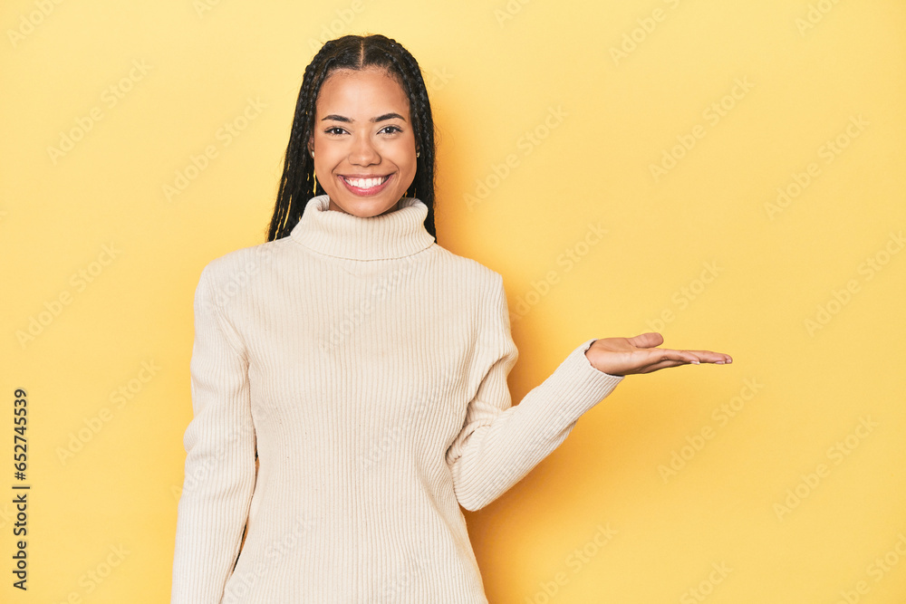 Young Indonesian woman on yellow studio backdrop showing a copy space on a palm and holding another hand on waist. Young Indonesian woman on yellow studio backdrop showing a copy space on a palm and holding another hand on waist.