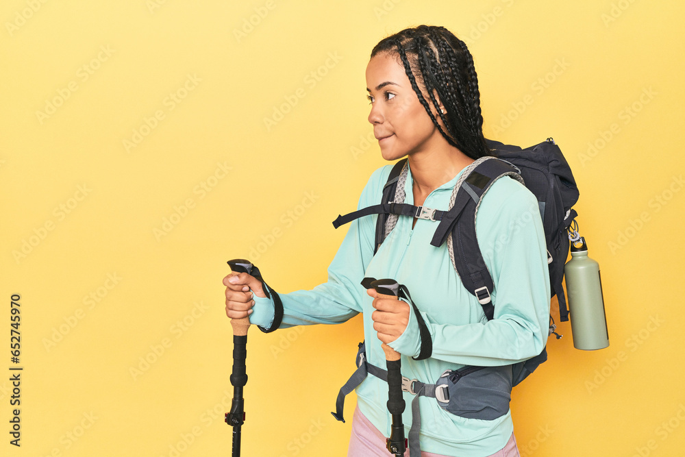 Indonesian hiker with backpack and poles on yellow