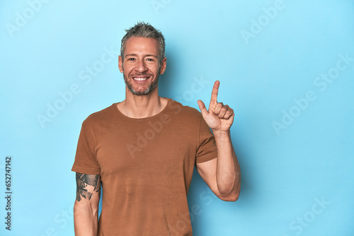 Middle-aged caucasian man on blue backdrop showing number one with finger.