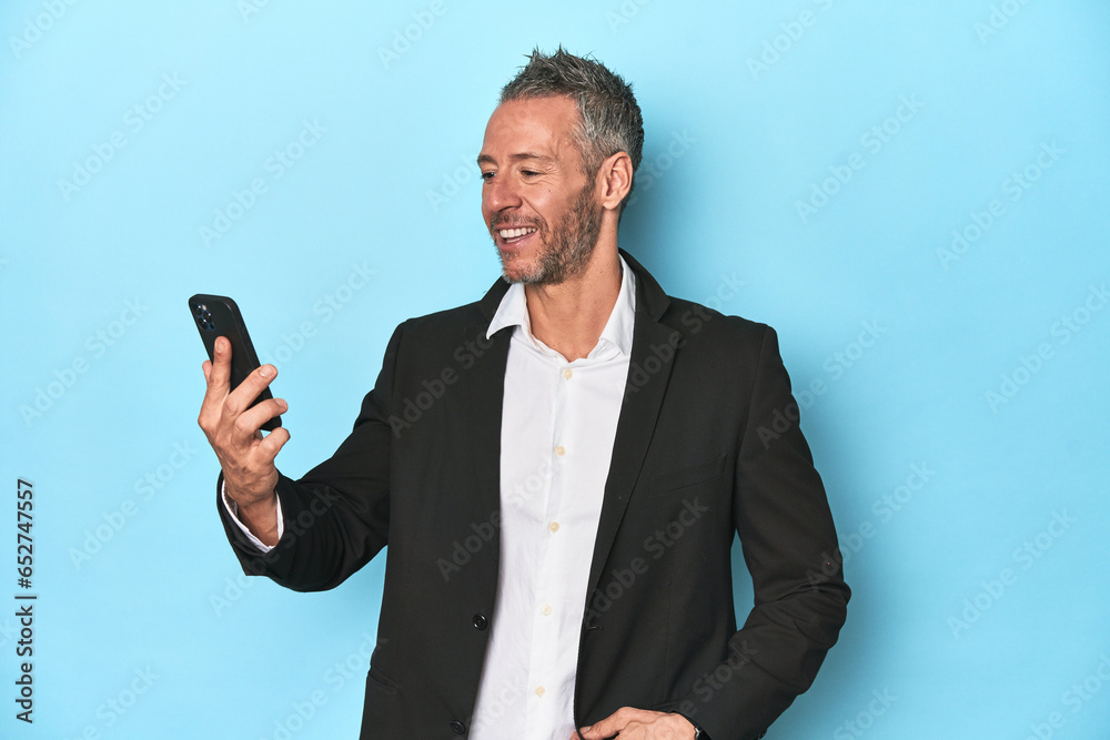 Businessman in suit making a videocall on blue backdrop Businessman in suit making a videocall on blue backdrop