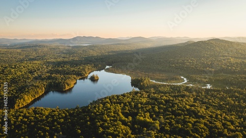 Drone view of lake surrounded by lush green forest in the sunlight next to mountains © Austin Weidhuner/Wirestock Creators