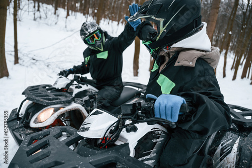 Making high five. Two people are riding ATV in the winter forest