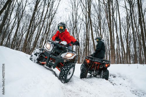 On the off road. Two people are riding ATV in the winter forest