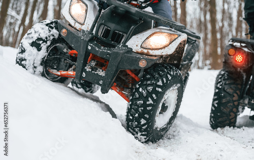 Close up view of vehicles. Two people are riding ATV in the winter forest
