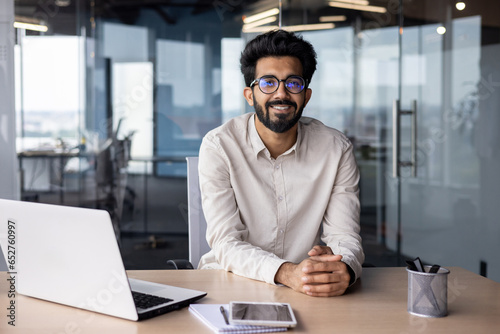Portrait of a young Indian male designer, engineer sitting in the office at the table and looking at the camera