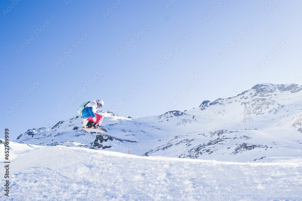 Person snowboarding on the slope of the mountain with a blue sky in the background