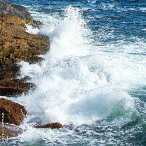 Closeup shot of foamy ocean waves crashing on a cliff on a sunny day
