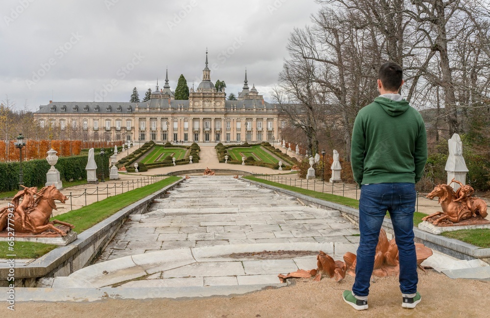 Young man in jeans and sweatshirt has spectacular views of the Royal Palace of San Idelfonso. Spain