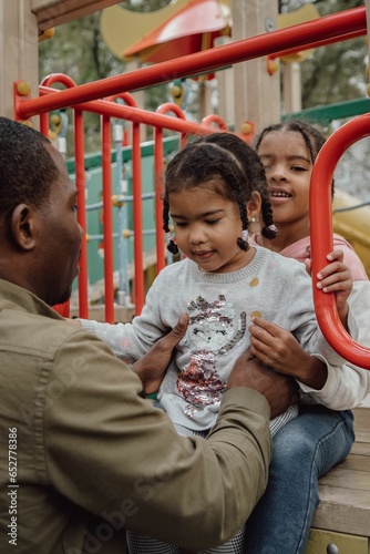 Vertical shot of an Afro-American father playing with his daughter in a playground