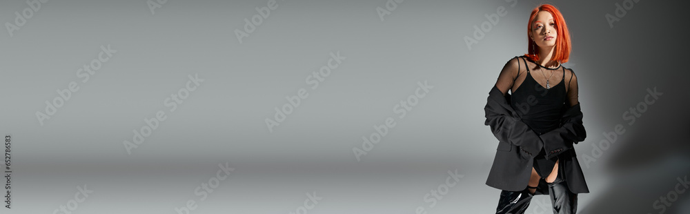 banner of stylish asian woman with red hair posing in bold outfit on grey, edgy look in black latex banner of stylish asian woman with red hair posing in bold outfit on grey, edgy look in black latex