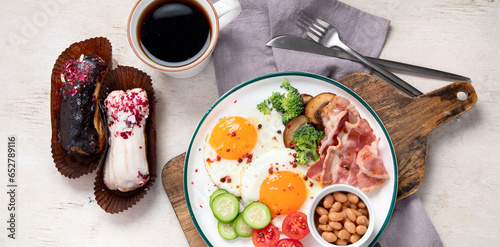 Traditional Englis breakfast plate with bacon strips, sunny side up eggs, vegetables and cake on light background photo