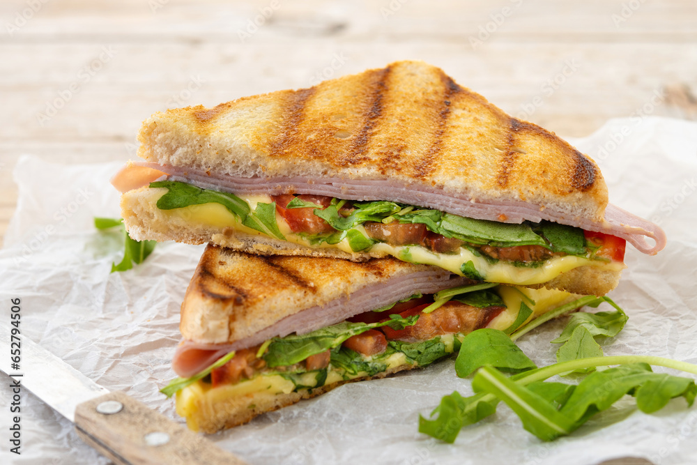 Panini sandwich with ham, cheese, tomato and arugula on wooden table Panini sandwich with ham, cheese, tomato and arugula on wooden table