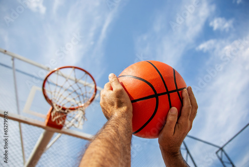 Close-up of basketball player holding ball while standing against blue sky. Success, scoring, winning and achieve the goal concept © Yelena