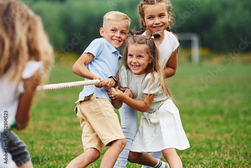 Smiling, playing tug of war game. Kids are having fun on the field at daytime together